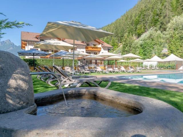 Piscina estiva con lettini, ombrelloni e montagne verdi sullo sfondo