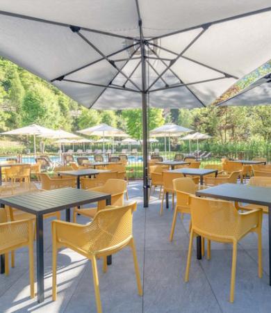 Terrazza soleggiata con sedie gialle, ombrelloni e vista paesaggio montano estivo