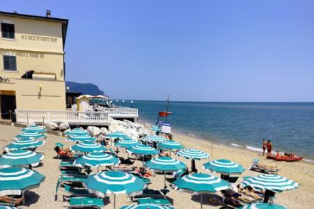 Spiaggia affollata con ombrelloni verdi e bianchi, vista mare e bagnini