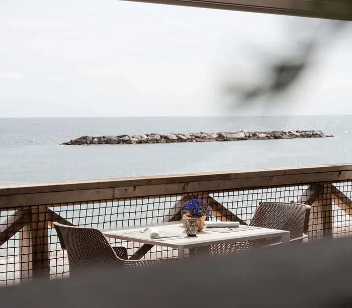 Tavolo apparecchiato e vista sul mare da una terrazza con balaustra in legno