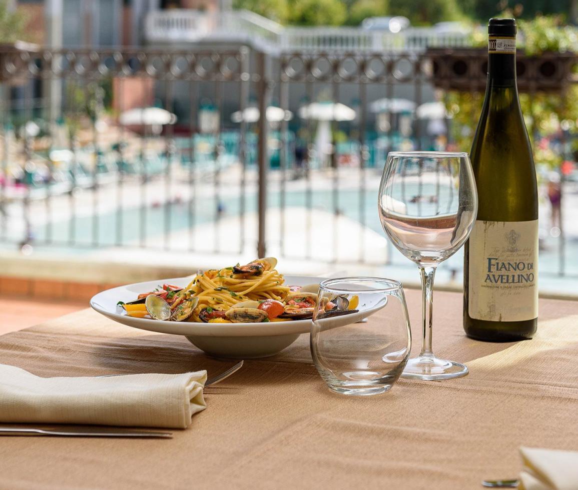 Pasta con vongole e vino su tavolo elegante, vista piscina soleggiata