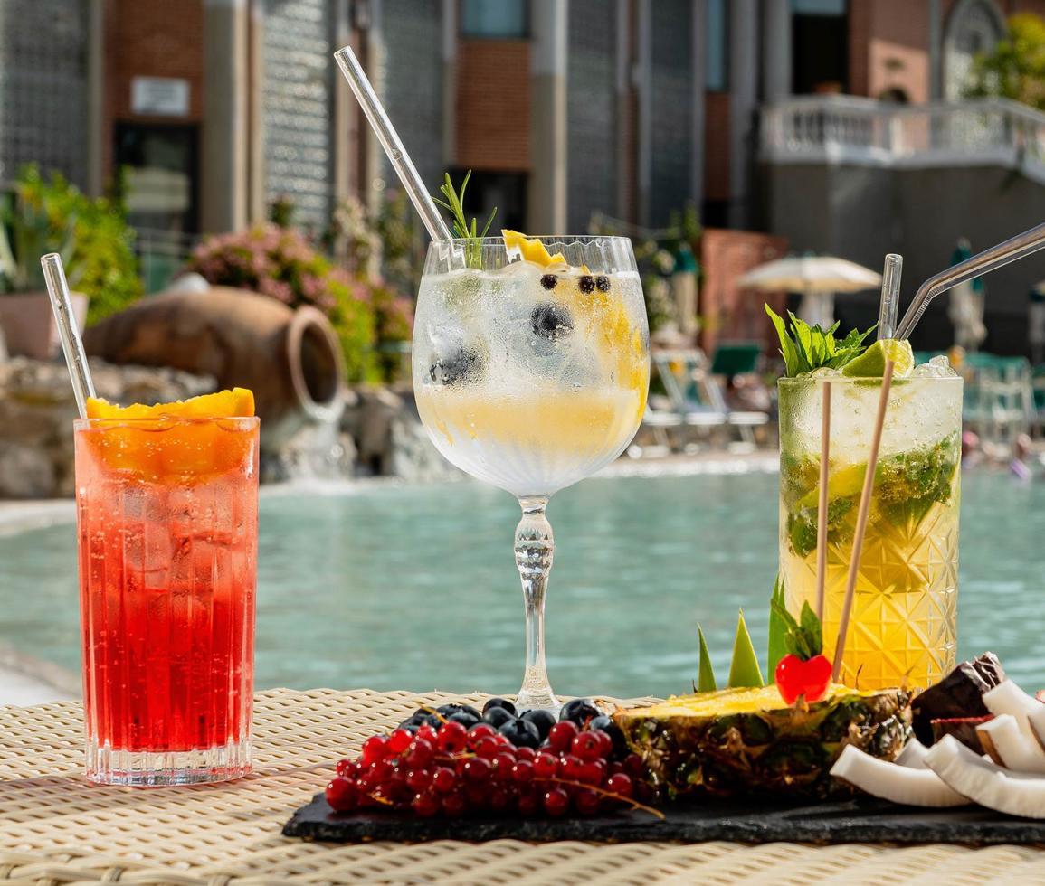 Cocktail colorati a bordo piscina, atmosfera estiva e frutta fresca esotica
