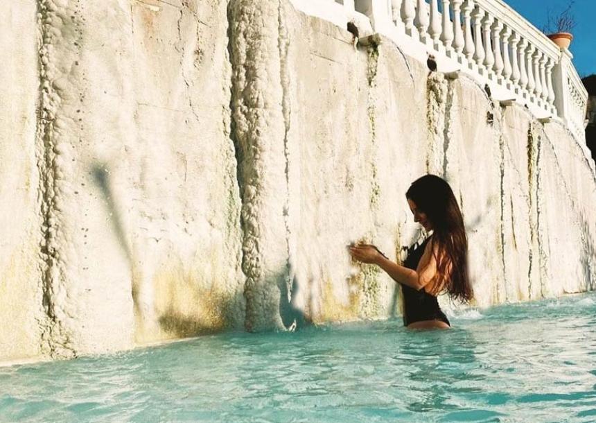 Donna in piscina termale, tocca una parete bianca sotto il sole