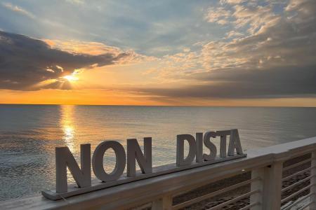 Tramonto sul mare con scritta NON DISTA su una ringhiera