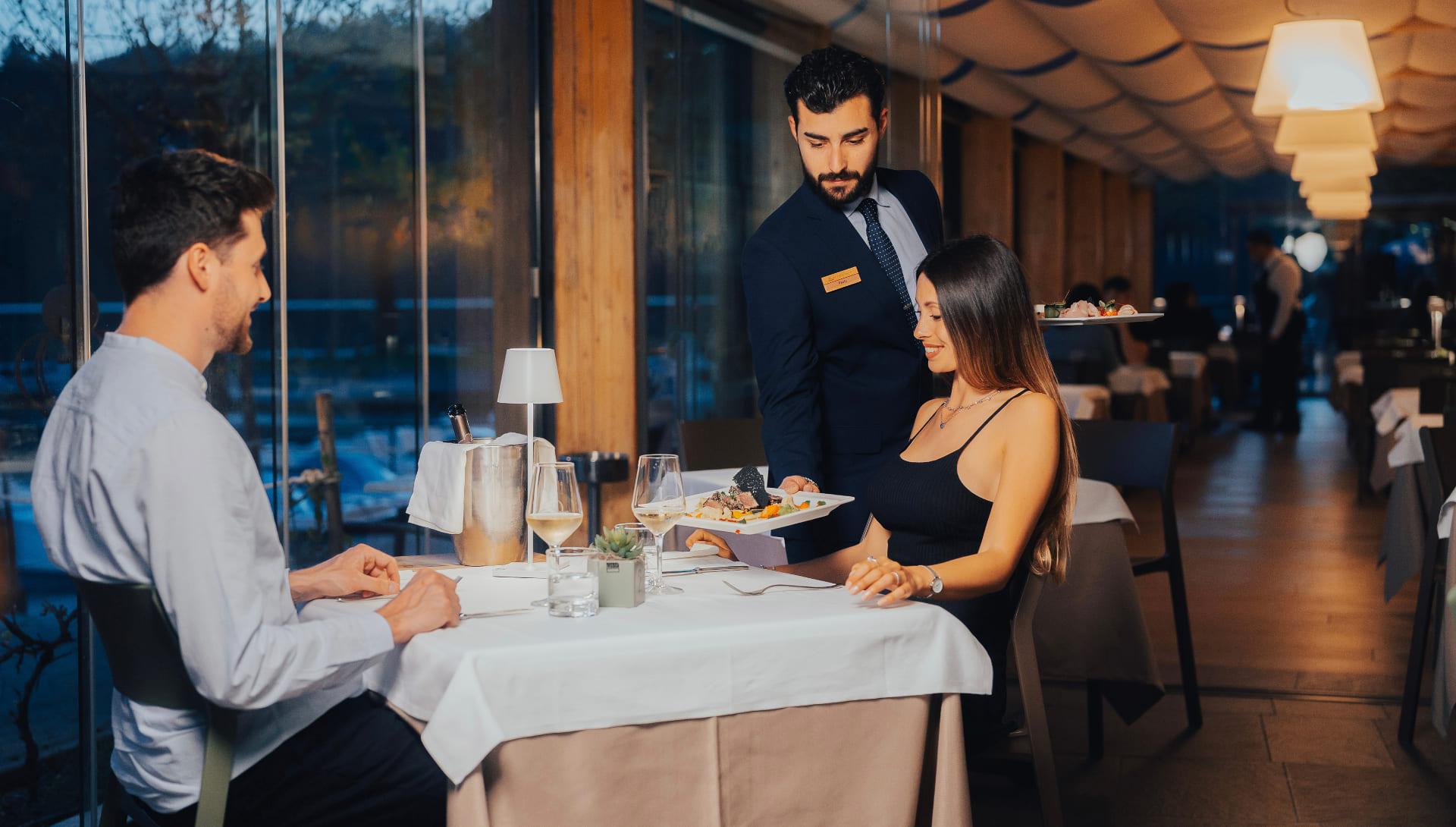 Cameriere serve piatti gourmet a una coppia nel ristorante elegante