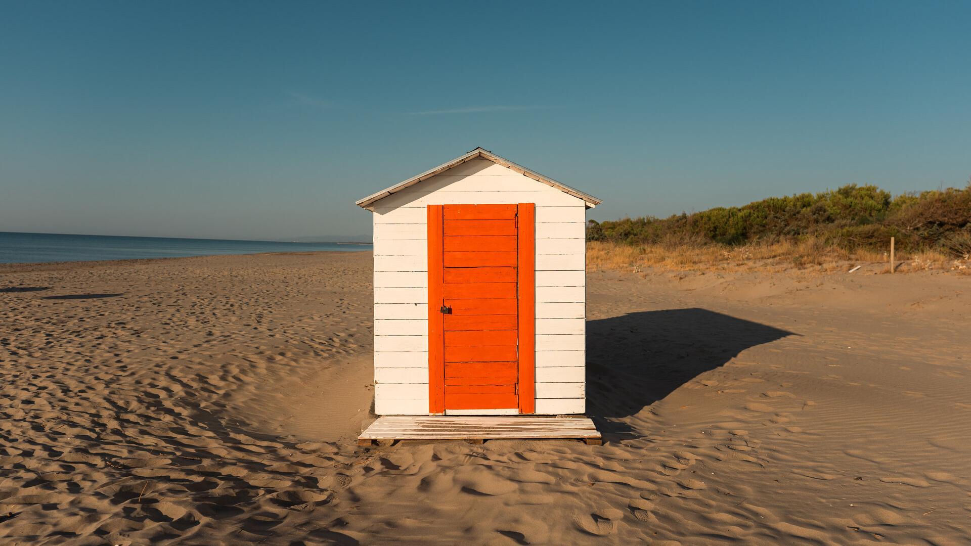 Coppia che si gode un pranzo in spiaggia con vino, sotto ombrelloni arancioni