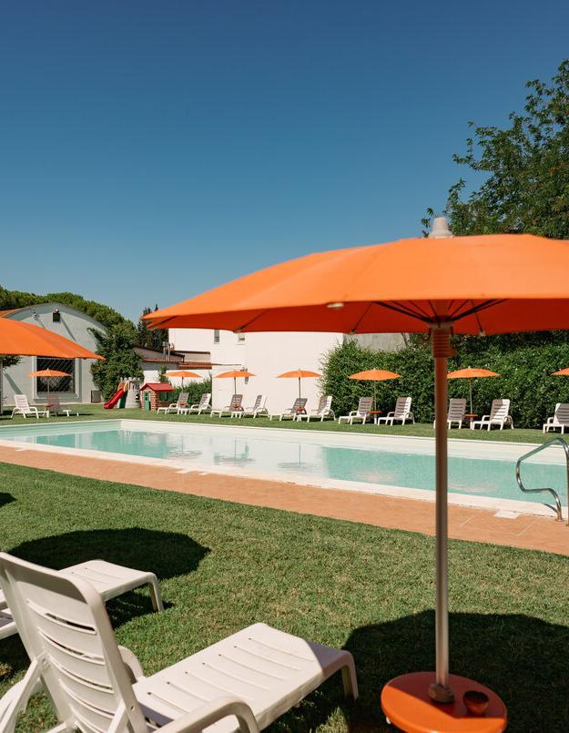 Piscina all'aperto con ombrelloni arancioni e lettini su prato verde