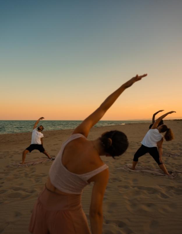 Gruppo di persone fa yoga sulla spiaggia al tramonto