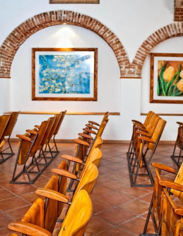 Sala con sedie in legno, archi in mattoni e quadri colorati alle pareti