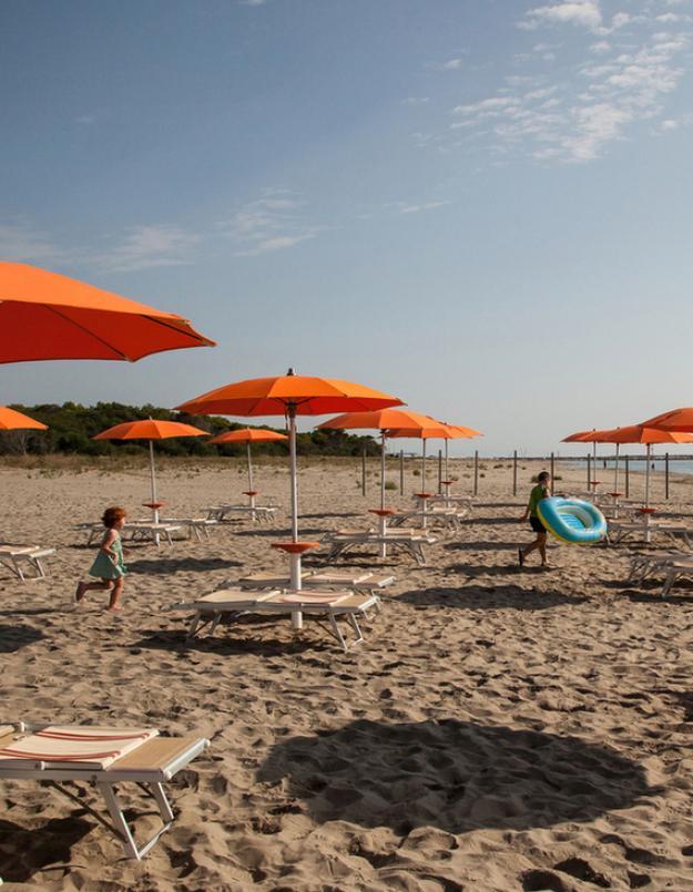 Spiaggia con ombrelloni arancioni, lettini e alcune persone sullo sfondo
