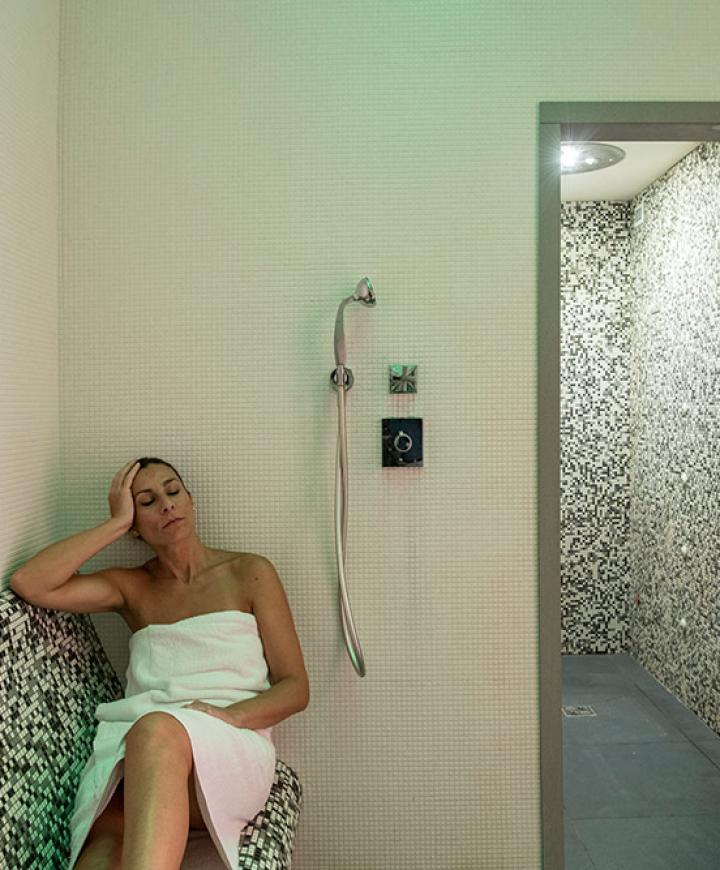 Donna rilassata in sauna, avvolta in un asciugamano, atmosfera serena e calda